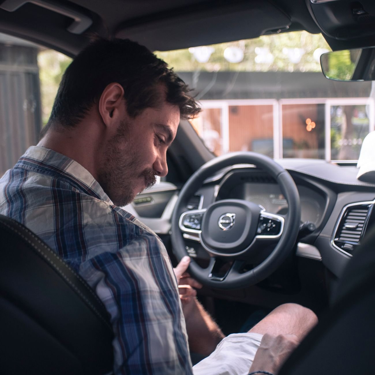 Casually dressed man smiling in the driver seat of a modern car interior.